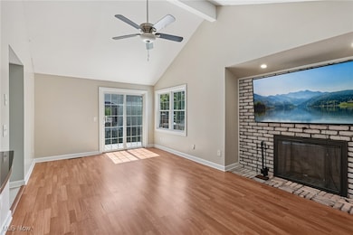Unfurnished living room featuring high vaulted ceiling, wood finished floors, beam ceiling, a brick fireplace, and a ceiling fan