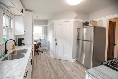 Kitchen with stainless steel refrigerator, sink, light stone countertops, white cabinetry, and light wood-type flooring