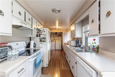 Kitchen featuring white appliances, washer and dryer, white cabinets, under cabinet range hood, and light countertops