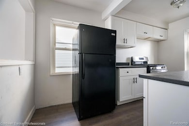 Kitchen with dark countertops, freestanding refrigerator, white cabinets, dark wood finished floors, and stainless steel range with gas cooktop