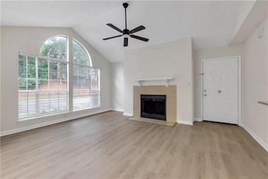 Unfurnished living room featuring vaulted ceiling, wood finished floors, a ceiling fan, and a tile fireplace