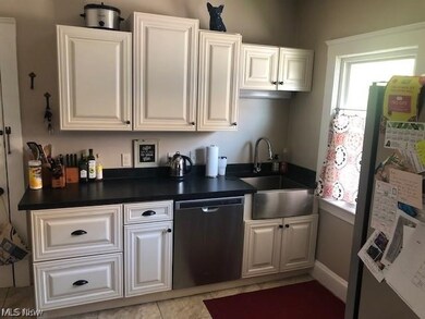 Kitchen with stainless steel appliances, white cabinetry, sink, and light tile flooring