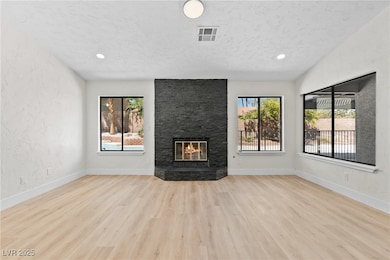 Unfurnished living room with a textured wall, light wood-style floors, a fireplace, a textured ceiling, and recessed lighting