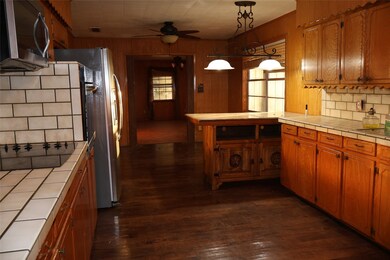 Kitchen featuring tile counters, stainless steel appliances, brown cabinets, decorative backsplash, and ceiling fan