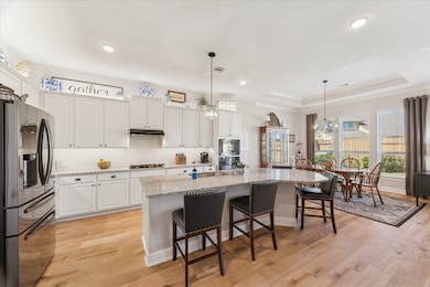 The kitchen has modern appliances, a granite island with bar seating, and white cabinets. It connects to a bright dining area with large windows and stylish lighting, ideal for entertaining.