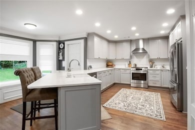 Kitchen with stainless steel appliances, wall chimney exhaust hood, a peninsula, ornamental molding, and a breakfast bar area