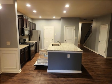 Kitchen with black gas range oven, a sink, stainless steel fridge, an island with sink, and recessed lighting