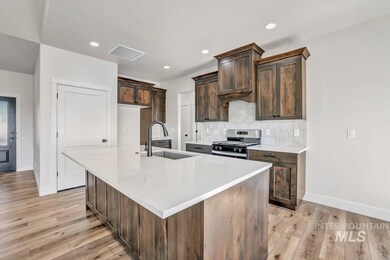 Kitchen with stainless steel range with gas stovetop, light wood finished floors, a kitchen island with sink, tasteful backsplash, and dark brown cabinetry