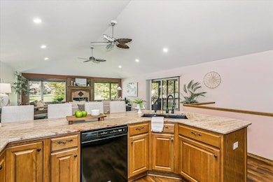 Kitchen with brown cabinetry, light stone countertops, open floor plan, dishwasher, and dark wood-type flooring