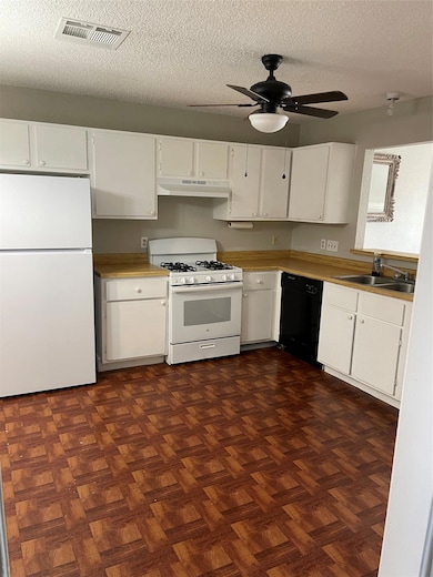 Kitchen with black refrigerator, white range with gas stovetop, a textured ceiling, white cabinets, and a ceiling fan