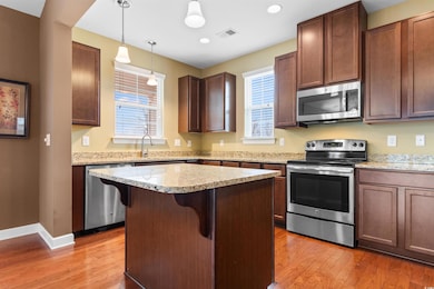Kitchen with a breakfast bar area, wood-type flooring, appliances with stainless steel finishes, a kitchen island, and pendant lighting