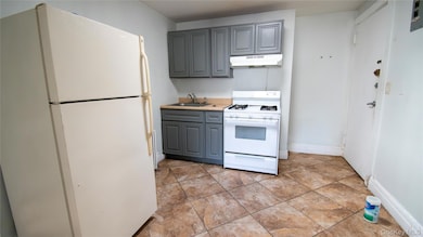 Kitchen with white appliances, gray cabinets, light countertops, under cabinet range hood, and light tile patterned floors