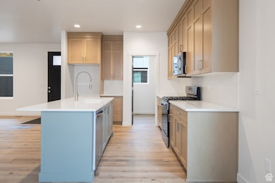 Kitchen with stainless steel appliances, decorative backsplash, light stone countertops, a center island with sink, and light wood-style floors
