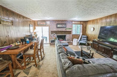 Living room with wood walls, a textured ceiling, light colored carpet, and a brick fireplace