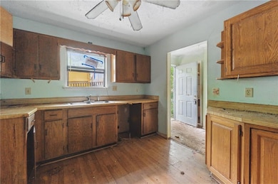 Kitchen with hardwood / wood-style floors, ceiling fan, light countertops, and brown cabinets