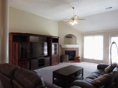 Carpeted living room featuring vaulted ceiling, a ceiling fan, crown molding, and a fireplace