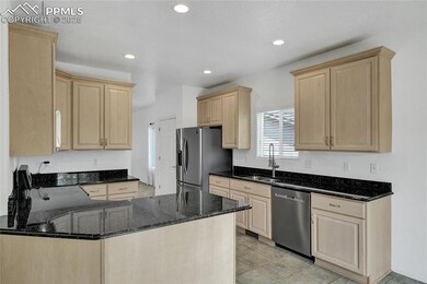 Kitchen with light brown cabinetry, stainless steel appliances, a sink, a peninsula, and dark stone countertops