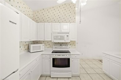 Kitchen with white appliances, light countertops, white cabinets, and wallpapered walls