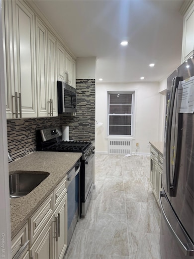 Kitchen with appliances with stainless steel finishes, light stone counters, decorative backsplash, recessed lighting, and radiator heating unit
