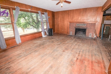 Unfurnished living room featuring wooden walls, a fireplace, a textured ceiling, wood finished floors, and ceiling fan