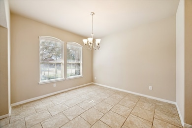 This photo showcases a bright, dining room with neutral-color walls and tiled flooring. It features a window with blinds and a simple overhead light fixture, creating a clean and versatile space suitable for dining or a sitting area.