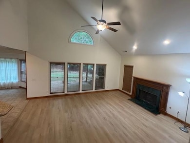 Unfurnished living room with high vaulted ceiling, baseboards, a fireplace, ceiling fan, and light wood-type flooring