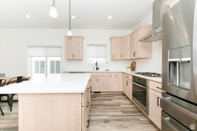 Kitchen with wall chimney range hood, a sink, appliances with stainless steel finishes, and light brown cabinets