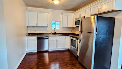 Kitchen featuring appliances with stainless steel finishes, white cabinets, dark countertops, and a textured ceiling