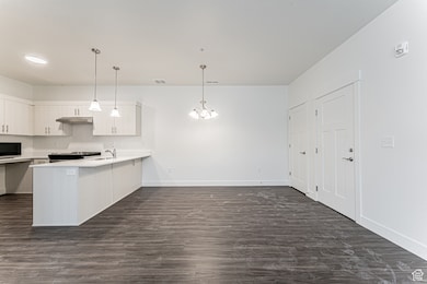 Kitchen featuring a sink, a peninsula, light countertops, white cabinets, and dark wood-style floors