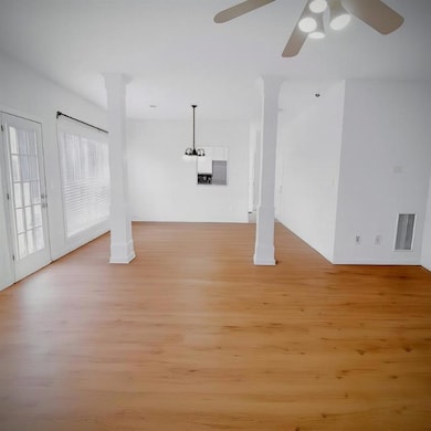 Unfurnished living room with light wood-style flooring, a ceiling fan, and ornate columns