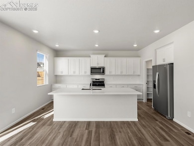Kitchen with stainless steel appliances, white cabinets, a center island with sink, dark wood-style flooring, and recessed lighting