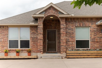 Property entrance featuring a shingled roof and brick siding