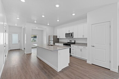 Kitchen featuring a center island with sink, appliances with stainless steel finishes, white cabinetry, light stone counters, and light wood-style flooring