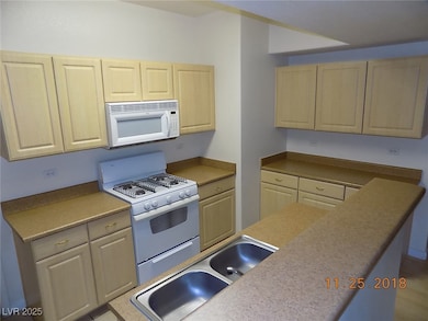 Kitchen with white appliances, light countertops, and light brown cabinetry