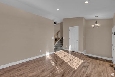 Unfurnished living room with wood finished floors, stairway, recessed lighting, and a chandelier