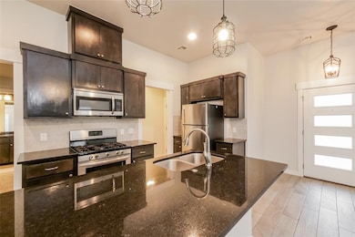 Kitchen featuring stainless steel appliances, decorative backsplash, dark brown cabinetry, and pendant lighting