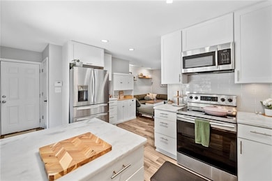 Kitchen with appliances with stainless steel finishes, stone countertops, tasteful backsplash, white cabinetry, upgraded dishwasher, and wood-style floors.