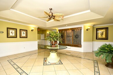 Tiled living area featuring a tray ceiling, inlaid floor details, wainscoting, a ceiling fan, and crown molding
