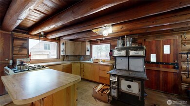 Rustic log cabin kitchen with vintage wood-burning stove, modern gas cooktop, and warm wood finishes throughout.