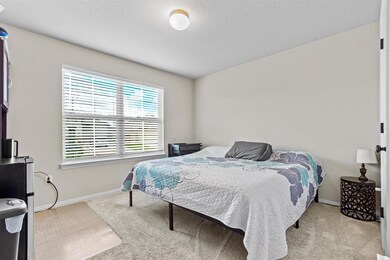 Bedroom with freestanding refrigerator, light carpet, and a textured ceiling