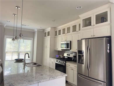 Kitchen with stainless steel appliances, light stone countertops, hanging light fixtures, glass insert cabinets, and backsplash
