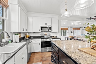 Kitchen with appliances with stainless steel finishes, white cabinetry, decorative light fixtures, light wood-style flooring, and tasteful backsplash