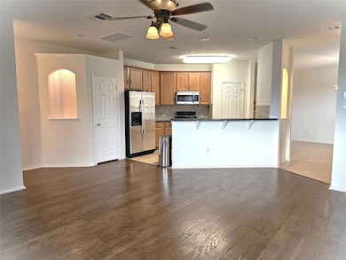 Kitchen featuring backsplash, brown cabinetry, appliances with stainless steel finishes, open floor plan, and dark wood-style flooring