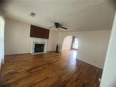 Unfurnished living room featuring ceiling fan, arched walkways, wood finished floors, a textured ceiling, and a fireplace