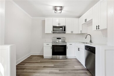 Kitchen featuring stainless steel appliances, light wood-style floors, white cabinetry, ornamental molding, and light stone counters