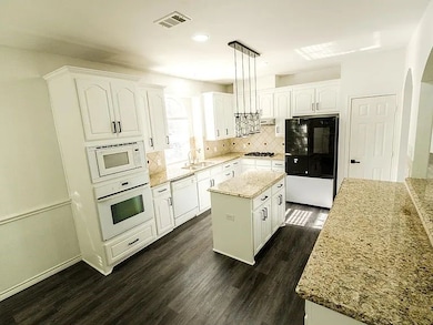 Kitchen with white cabinets, tasteful backsplash, decorative light fixtures, dark wood finished floors, and recessed lighting