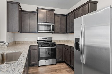 Kitchen with stainless steel appliances, dark brown cabinetry, light wood-type flooring, and light stone counters