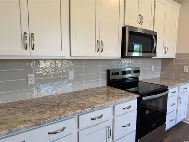Kitchen featuring appliances with stainless steel finishes, light stone countertops, white cabinets, and tasteful backsplash