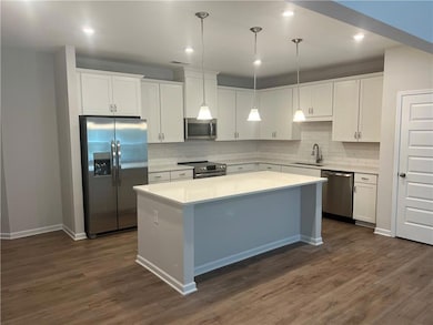 Kitchen featuring stainless steel appliances, white cabinetry, a kitchen island, pendant lighting, and tasteful backsplash