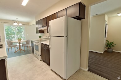 Kitchen featuring white appliances, light countertops, dark brown cabinetry, a chandelier, and a textured ceiling